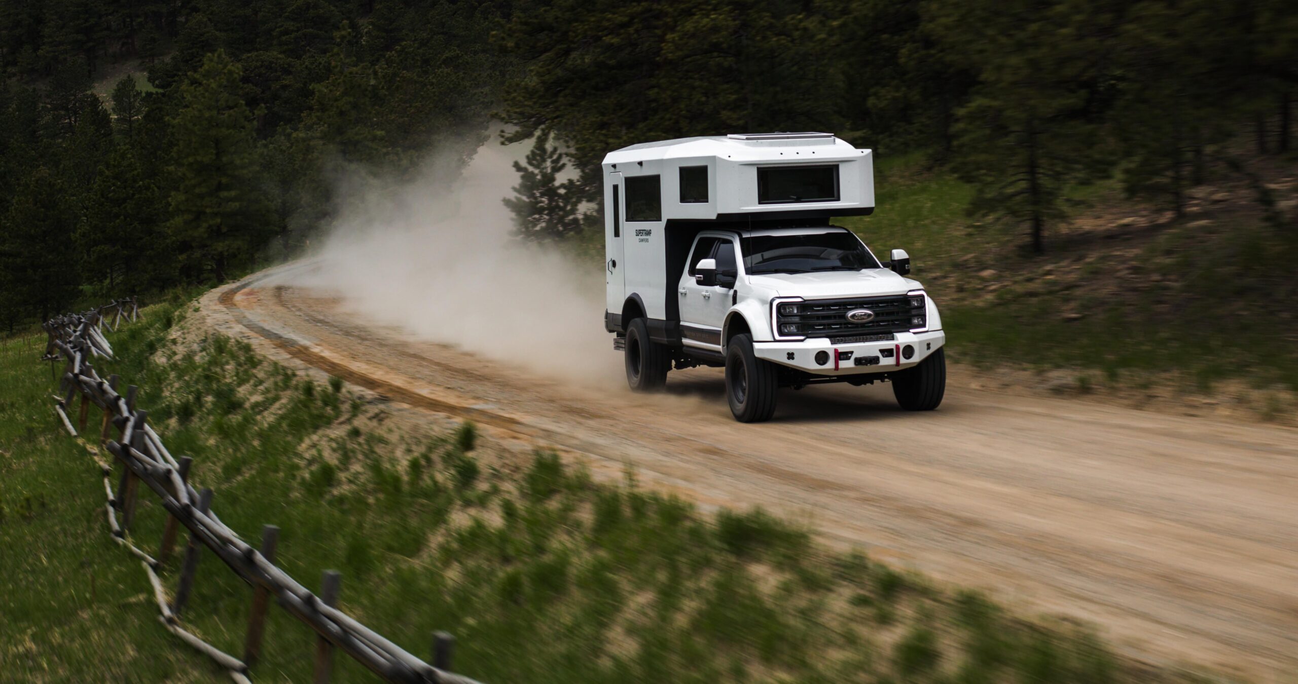 white Overland truck with camper top driving down dusty road