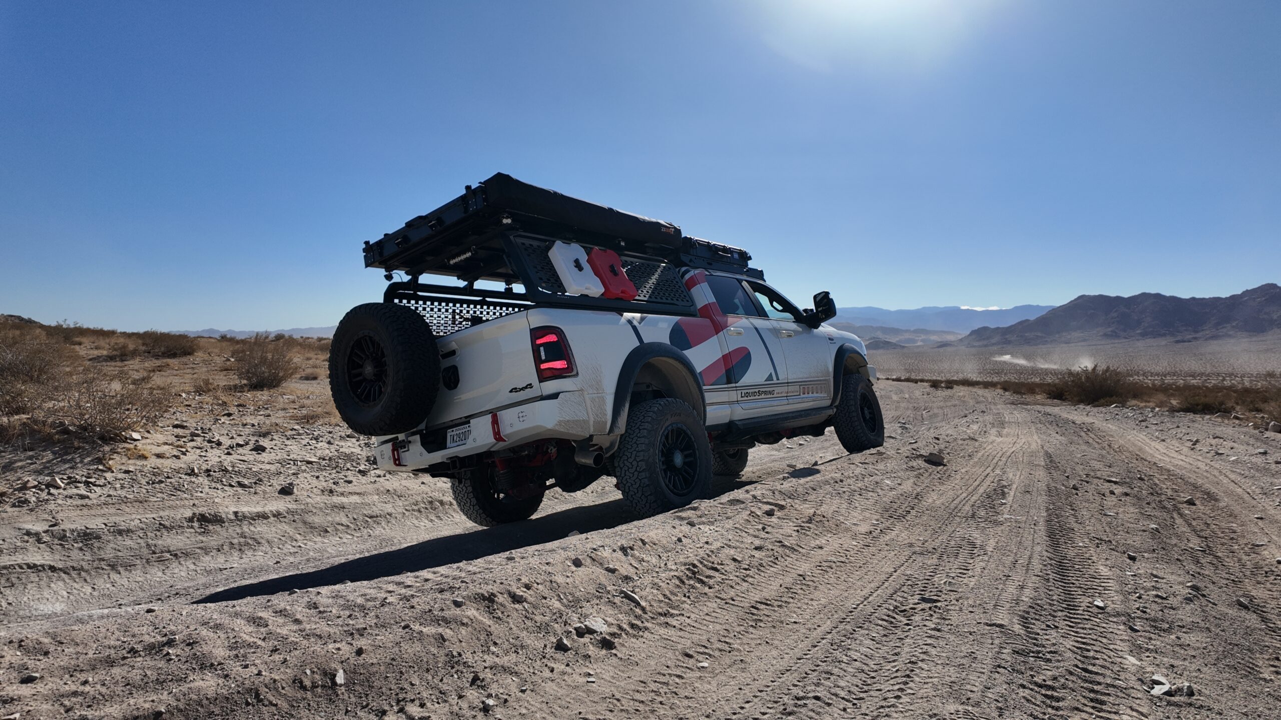 Adventure truck with liquid spring suspension off-roading in a desert with blue sky