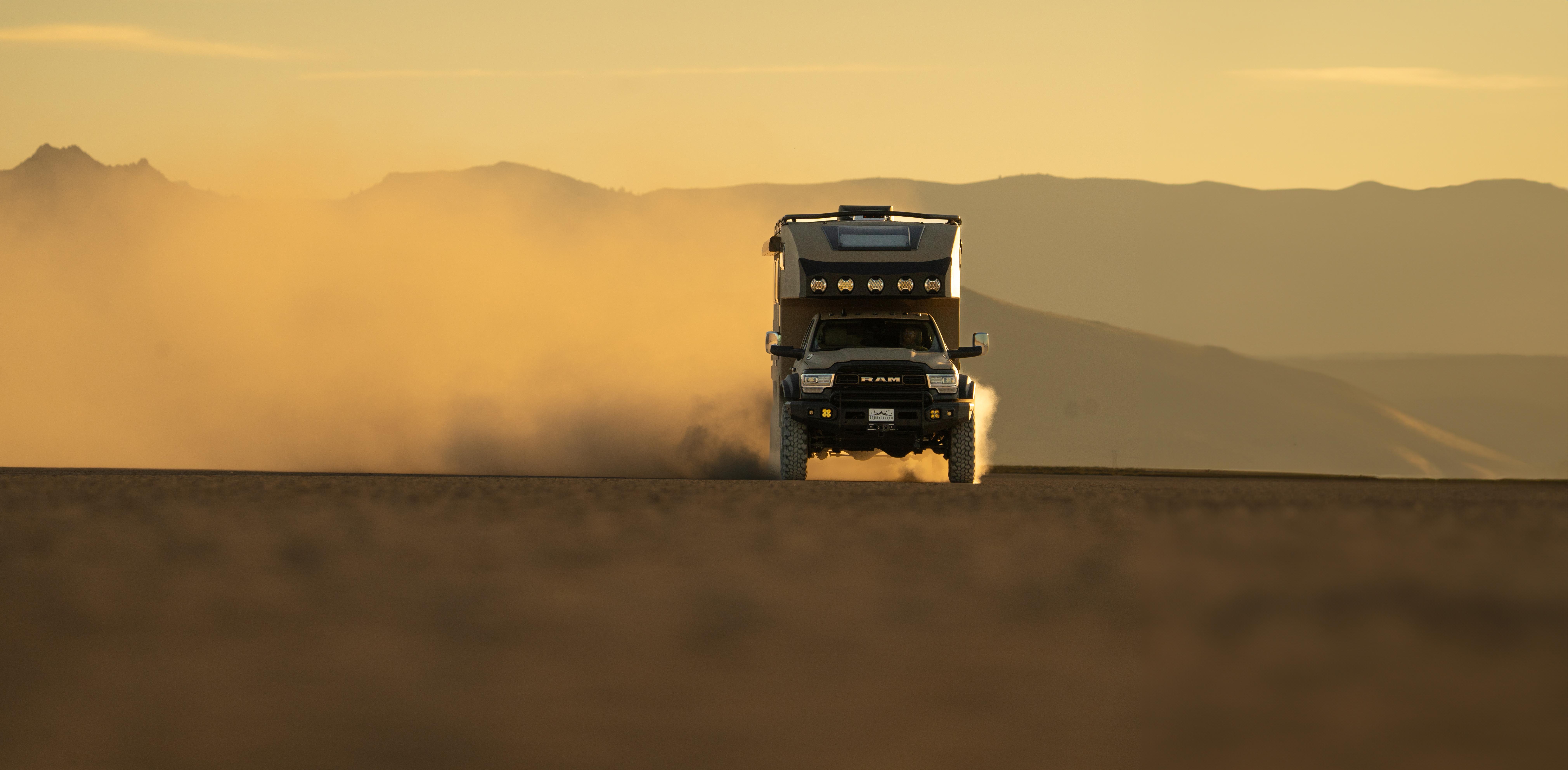Storyteller Overland truck driving through dust with the sunset orange