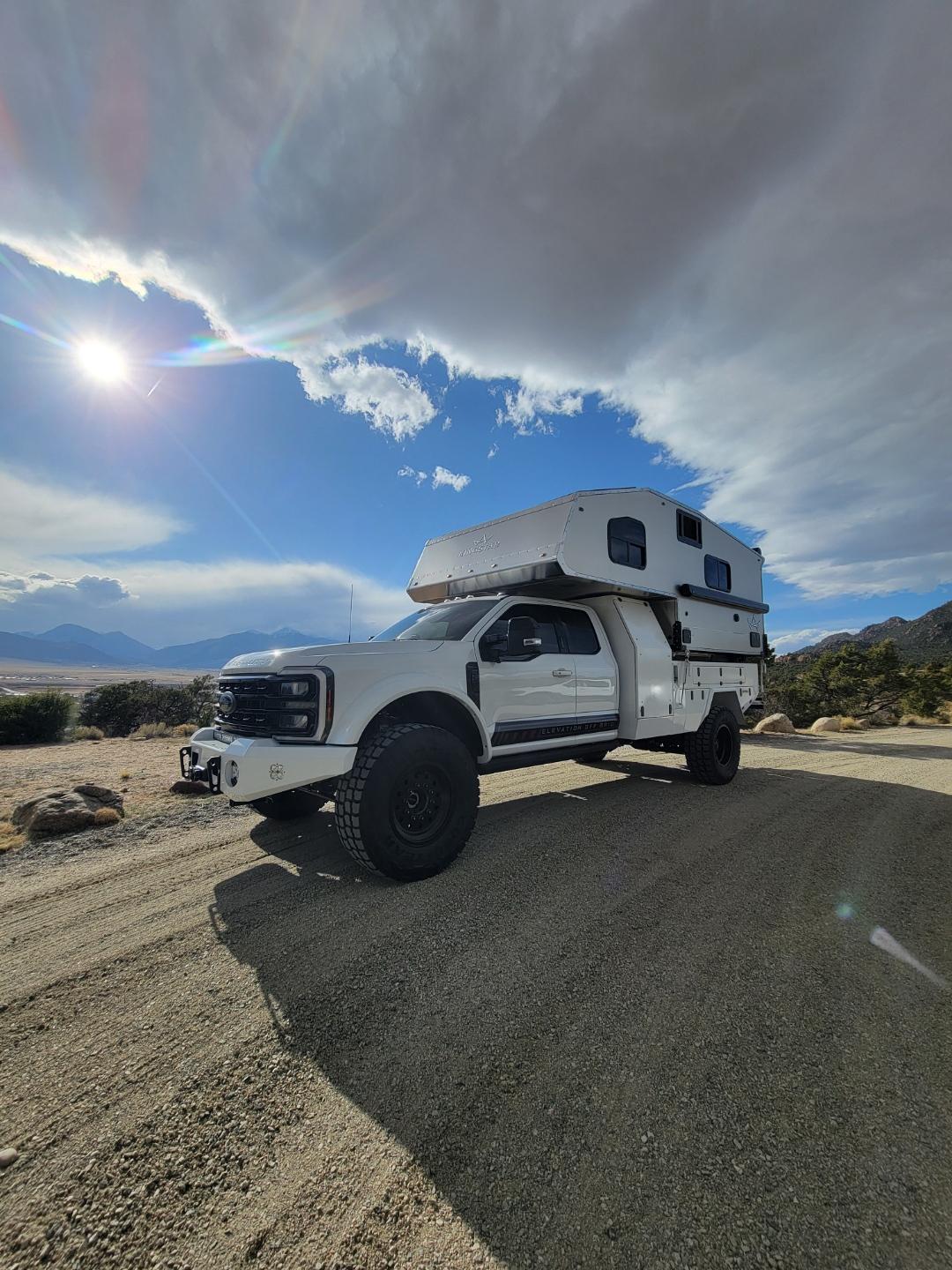 White F550 Truck Camper parked on dirt road in front of sun 
